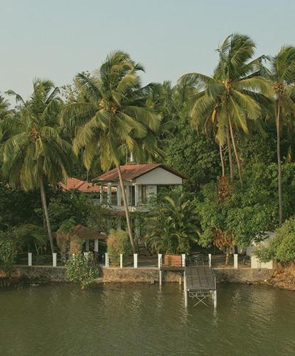 a house on the shore of a lake with palm trees at Bellevue Homestay - Ayurvedic Wellness Centre in Kozhikode