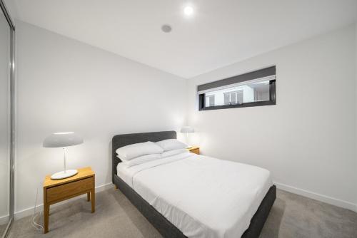 a white bedroom with a bed and a table with a lamp at Chic Inner-City 2-Bed Abode with Pool Gym & Sauna in Canberra