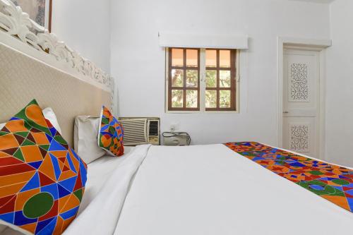 a white bedroom with a white bed with colorful pillows at FabHotel Prime Fair stayz in Goa