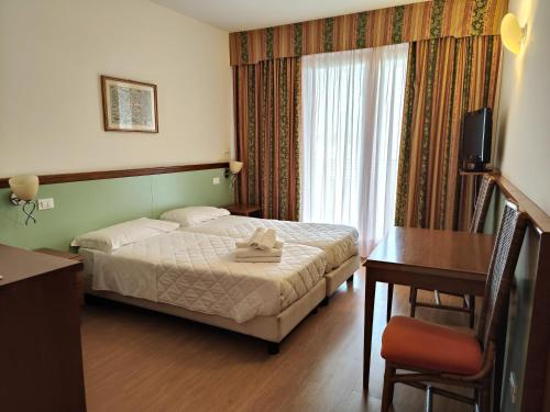 Cette chambre comprend un lit, un bureau et une fenêtre. dans l'établissement Hotel Il Guscio, à Grado