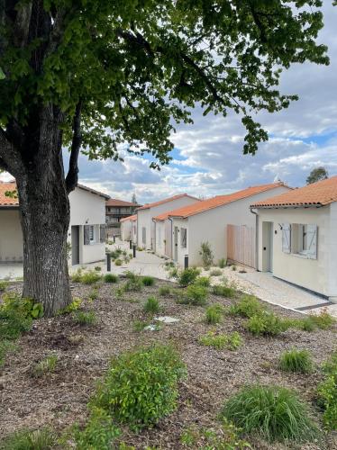 une rangée de bâtiments blancs avec un arbre dans l'établissement Résidence Grand Tilleul, à Jonzac