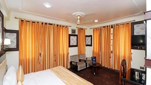 a bedroom with a bed and a tv and orange curtains at Hotel de elaaf in Srinagar