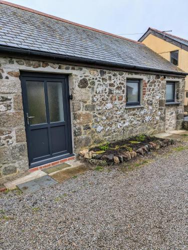 a stone house with a black door and two windows at Sterennyk in Helston