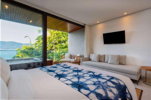 a bedroom with a bed and a couch and a television at Wyndham Ilhabela Casa Di Sirena in Ilhabela