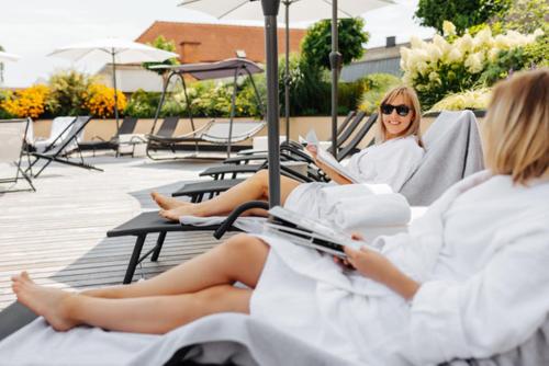 two women in white robes sitting in chairs reading books at Hotel Stainzerhof in Stainz