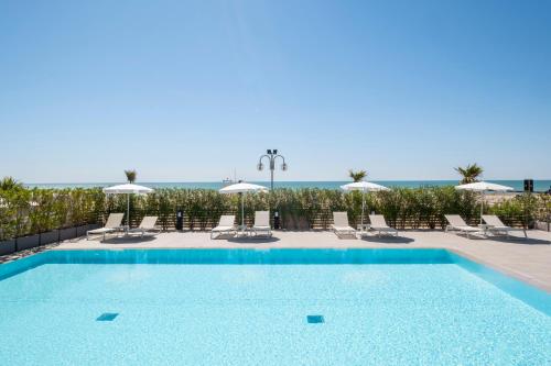 a swimming pool with chairs and umbrellas and the ocean at Vibra Tahiti Superior in Lido di Jesolo