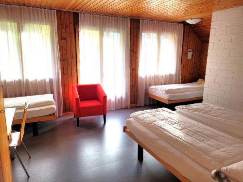 um quarto com 2 camas e uma cadeira vermelha em B&B Hotel Mattli Übernachtung Frühstück em Morschach