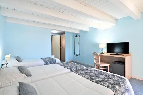 a room with two beds and a desk with a television at Cala Della Torre Resort in La Caletta