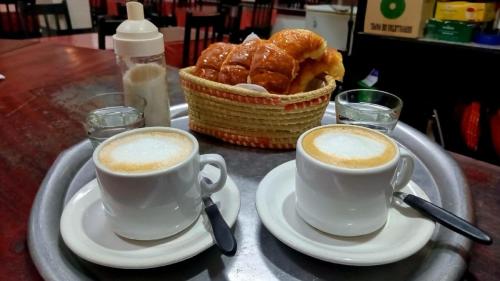 two cups of coffee and a basket of pastries on a table at Hostal Las Carretas in San Miguel de Tucumán