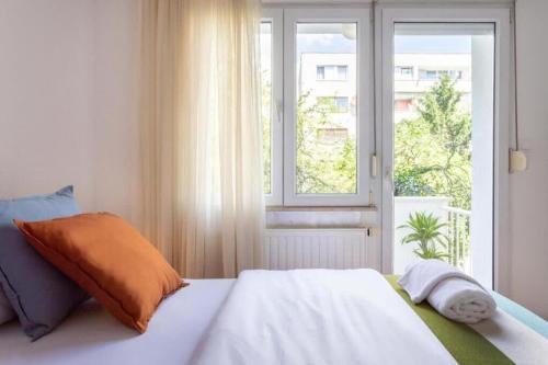 ein weißes Bett mit orangefarbenem Kissen und einem Fenster in der Unterkunft Kennedy Apartment URBAN STAY in Zagreb