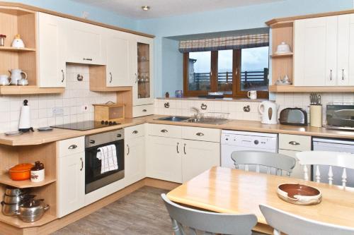 a kitchen with white cabinets and a wooden table at Covenanters Cottage , Balmaclellan in Castle Douglas