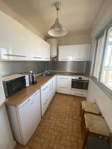 une cuisine avec des armoires blanches, un évier et un micro-ondes dans l'établissement Jolie appartement à 50m de la plage, à Narbonne-Plage