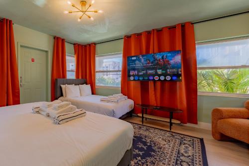 two beds in a room with orange curtains and a tv at Tropical Breeze in Clearwater Beach
