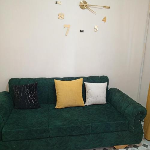 a green couch with pillows and a clock on the wall at Nakuru Residential and Fully Furnished apartments in Nakuru
