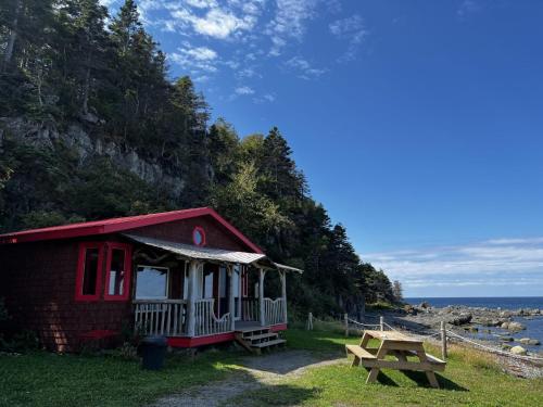 a red house with a picnic table and a bench at Auberge Festive Sea Shack in Sainte-Anne-des-Monts