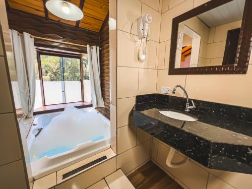 a bathroom with a tub with a sink and a mirror at Chalés Galinha Da Roça in Monte Verde