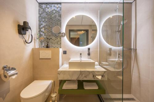 een badkamer met een toilet, een wastafel en een spiegel bij Leonardo Hotel Breda City Center in Breda