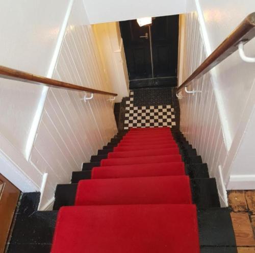 a staircase with a red carpet and a black door at Ness City Cottage in Inverness
