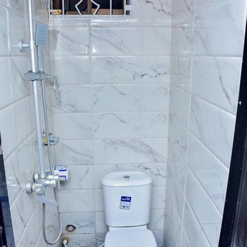THRIVEMAX HOTEL AND SUITE في لاغوس: حمام من البلاط الأبيض مع مرحاض ودش