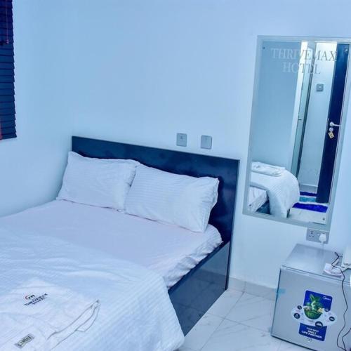 THRIVEMAX HOTEL AND SUITE في لاغوس: غرفة نوم بسرير أبيض مع مرآة