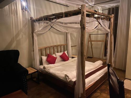 a bedroom with a canopy bed with red pillows at Afro Smile Hotel and Guest House in Jinja