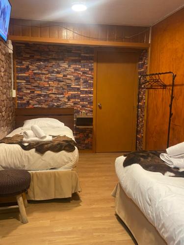 een slaapkamer met twee bedden en een bakstenen muur bij Hostal Queltehue in Ancud