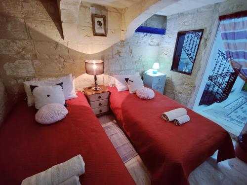2 Betten in einem Zimmer mit roter Bettwäsche und Kissen in der Unterkunft Traditional Maltese Townhouse in Rabat in Rabat