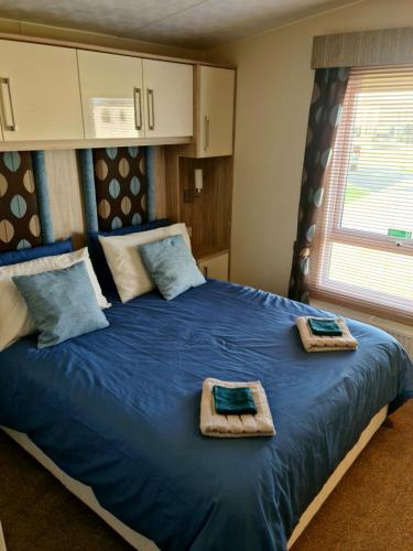 Un dormitorio con una cama azul con toallas. en Golden Anchor Caravan Park, Europa Sequoia Private Static Caravan Hire on Wildflower Meadow, en Chapel St. Leonards