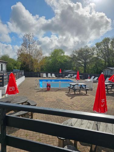 um grupo de mesas de piquenique com guarda-sóis vermelhos ao lado de uma piscina em PB6 em Bettws-Evan