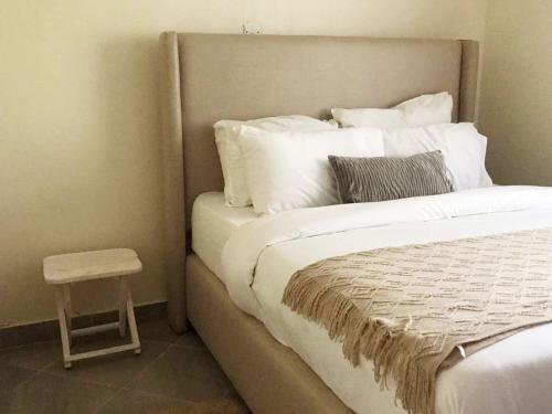 Una cama con almohadas blancas y un taburete en una habitación en Summer Homes Bungoma, en Bungoma