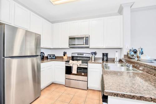 a kitchen with white cabinets and a stainless steel refrigerator at 3BR Condo - Games Hot Tub Sauna - Near Disney in Orlando