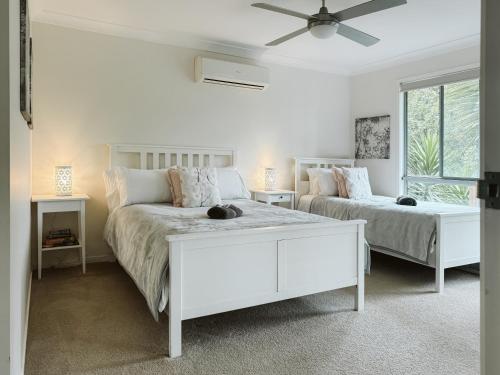 a white bedroom with two beds and a window at Kookaburra 2-Bedroom at On Burgum Pond Cottages in Maleny