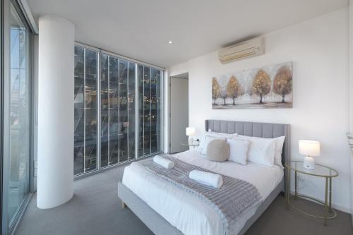 sypialnia z dużym białym łóżkiem i oknami w obiekcie Generous 2br2ba Docklands Free Parkingpool w Melbourne