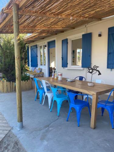 une table en bois et des chaises bleues sous un pavillon dans l'établissement Cabanon bohème les pieds dans le sable et en première ligne de mer, à Marseillan