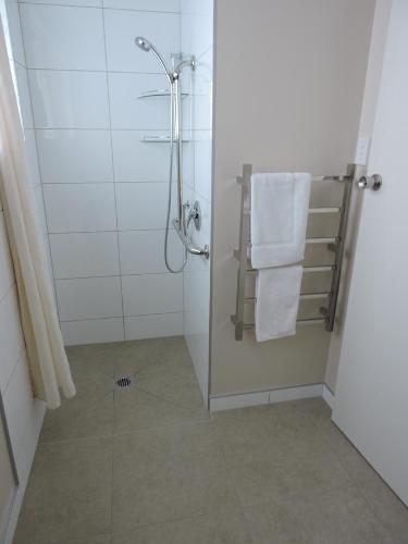 ein Bad mit einer Dusche und weißen Handtüchern in der Unterkunft Maple Lodge Motel in Matamata
