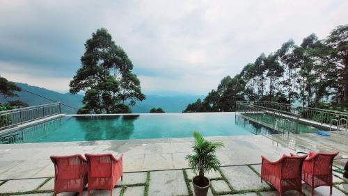 a pool with red chairs and mountains in the background at Fragrant Nature Munnar - A Five Star Classified Hotel in Munnar