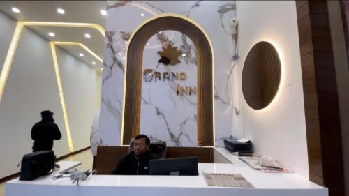 DatiaHotel Grand Inn的一名男子坐在商店前的办公桌前