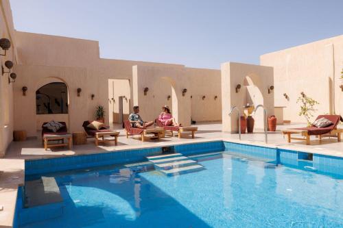 two people sitting in chairs next to a swimming pool at True Beach Resort in Marsa Alam City