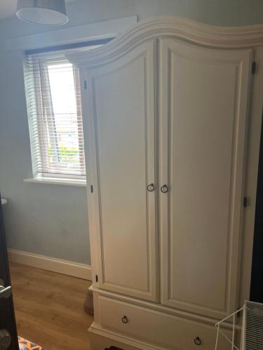 einen weißen Schrank in einem Zimmer mit Fenster in der Unterkunft Cozy single room in private home in Dagenham