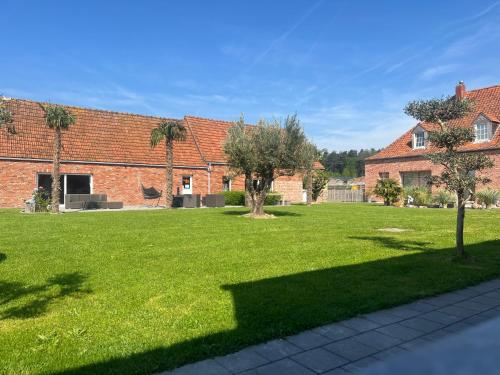 a green yard with trees and a brick building at B&B DeSo in Zonnebeke