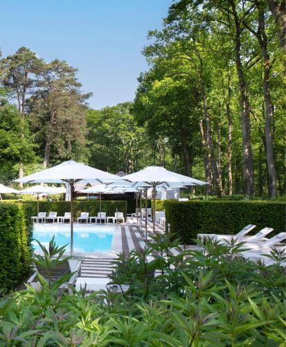 a pool with white umbrellas and chairs and tables at Relais & Chateaux Hotel Landgoed Het Roode Koper in Ermelo