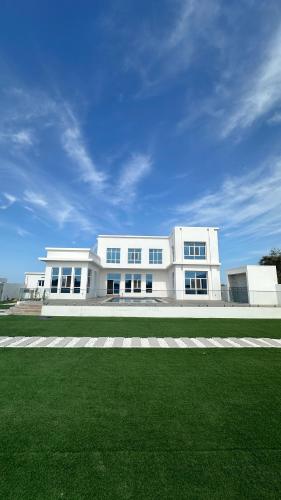 a white building with a green field in front of it at Palma Villa in Mussanah
