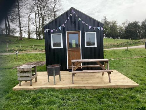 a small black house with a picnic table and a bench at Irongorge Camping in Telford