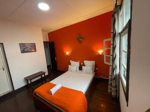 Habitación pequeña con cama y pared de color naranja en La Residence Mahasoa en Antsirabe