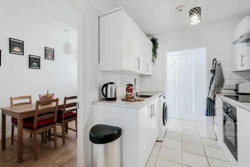 a kitchen with white cabinets and a table and chairs at 4 Bed House - Sleeps 6 - Garden Pets Wifi in London