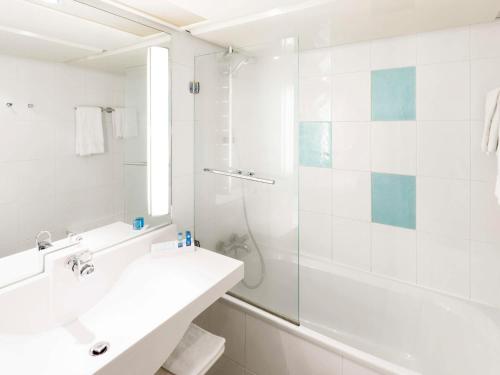 uma casa de banho branca com um lavatório e um chuveiro em Novotel Saint-Quentin en Yvelines em Magny-les-Hameaux
