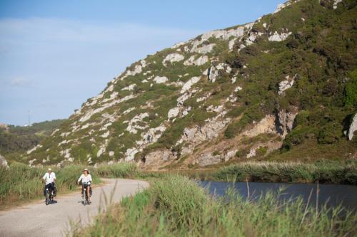 two people riding bikes on a road next to a mountain at Casa da Calçada in Maceira