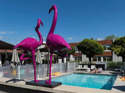 two pink flamingos standing next to a swimming pool at ibis Styles Lyon Bron Eurexpo in Bron