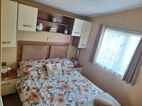 a bedroom with a bed with a floral comforter and a window at Countryside Caravan Accommodation - Abergele in Abergele