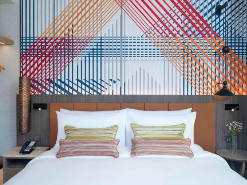 a bed with two pillows and a painting on the wall at Mercure Bangkok Surawong in Bangkok